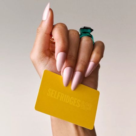 a hand with long pink nails holding a yellow gift card