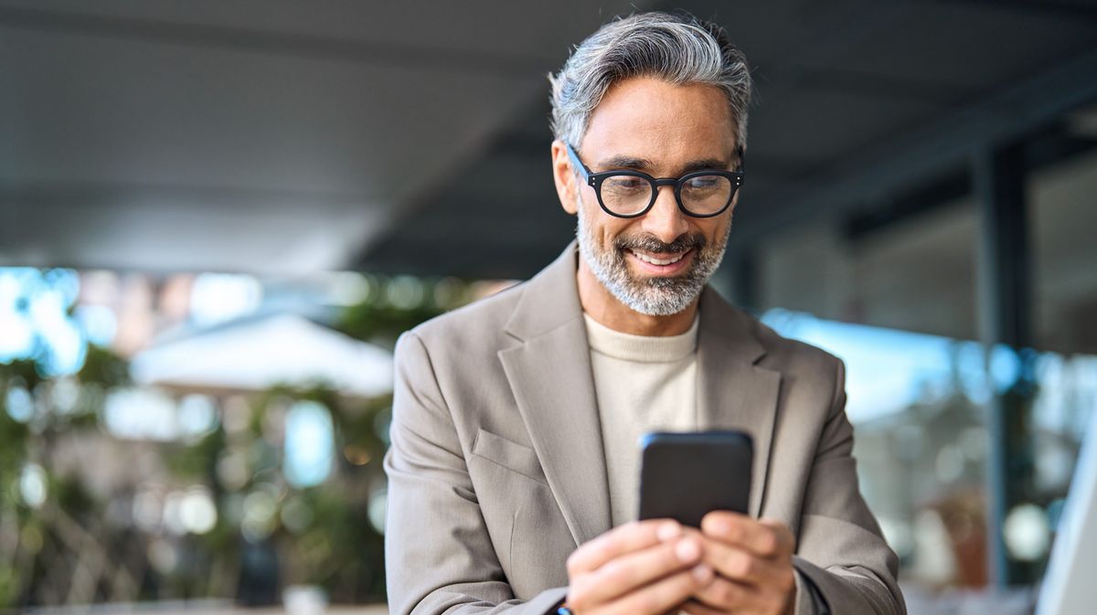 a silver-haired gentleman looks happily at his smartphone