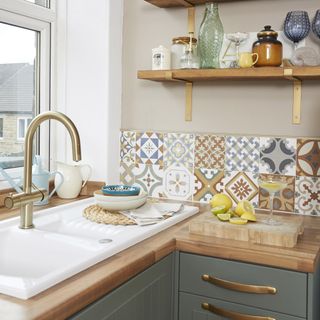 Kitchen with sage green cupboard doors, wood worktop and patterned tile splashback.