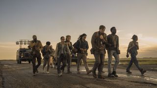 A group of young people walks down a long, dirt road at sunset