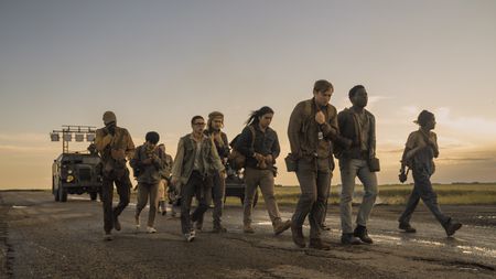A group of young people walks down a long, dirt road at sunset