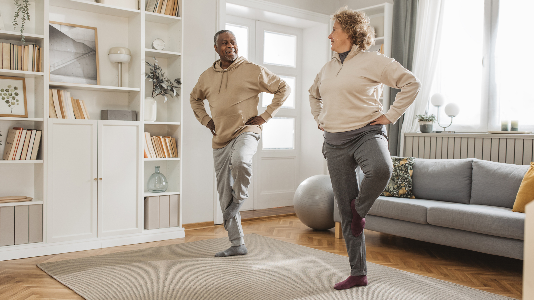 Man and woman balancing on one leg in living room