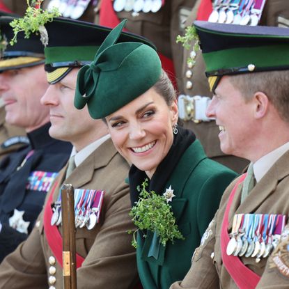 Princess Kate wearing a green coat sitting in a row of uniformed soldiers