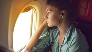 woman wearing a green shirt and earbuds looking our of an airplane window