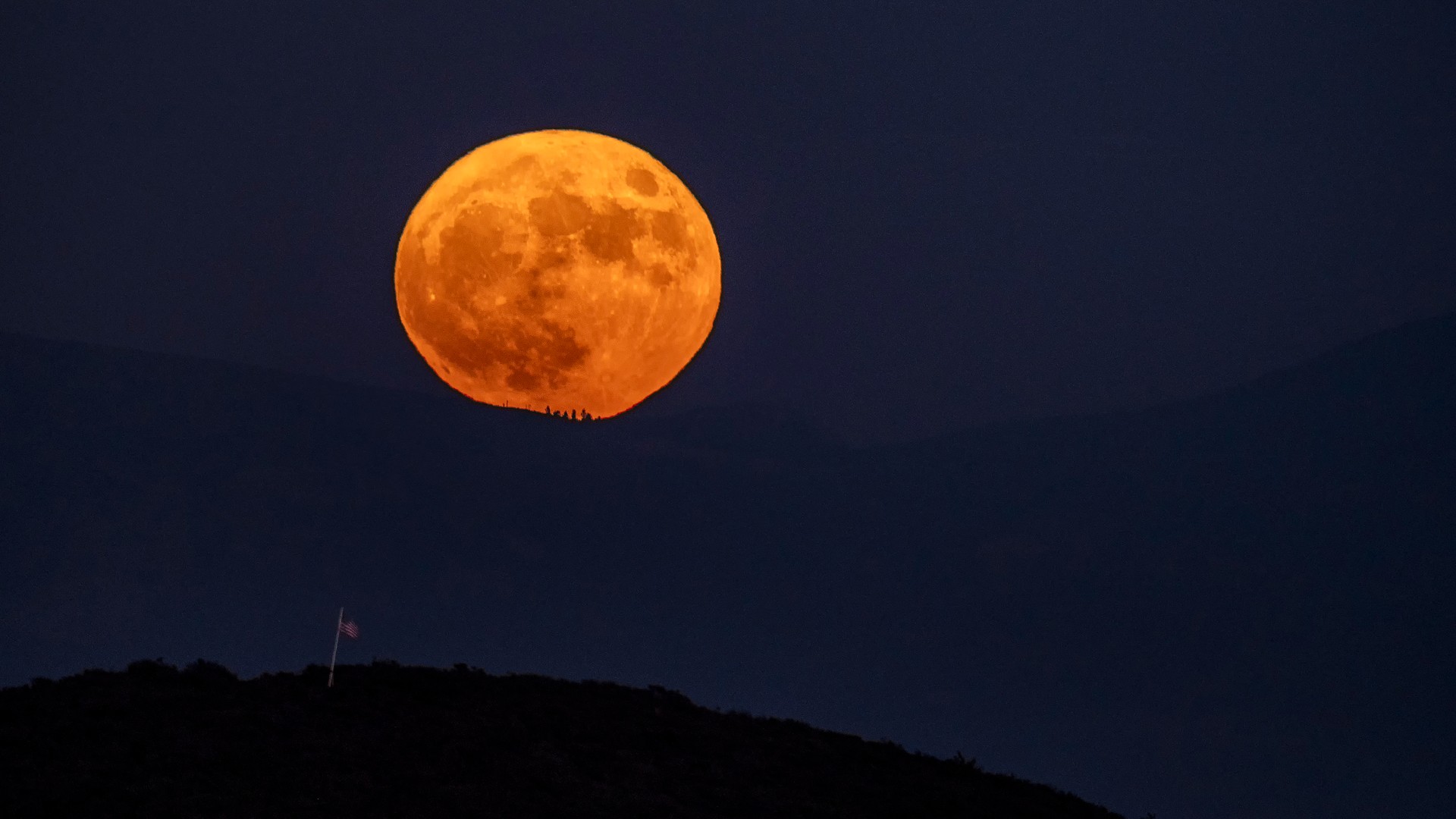 a bright full moon rises over a mountain range