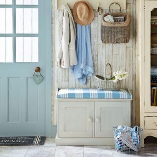 a hallway entrance with a blue door and striped blue and white bench with coats hanging above