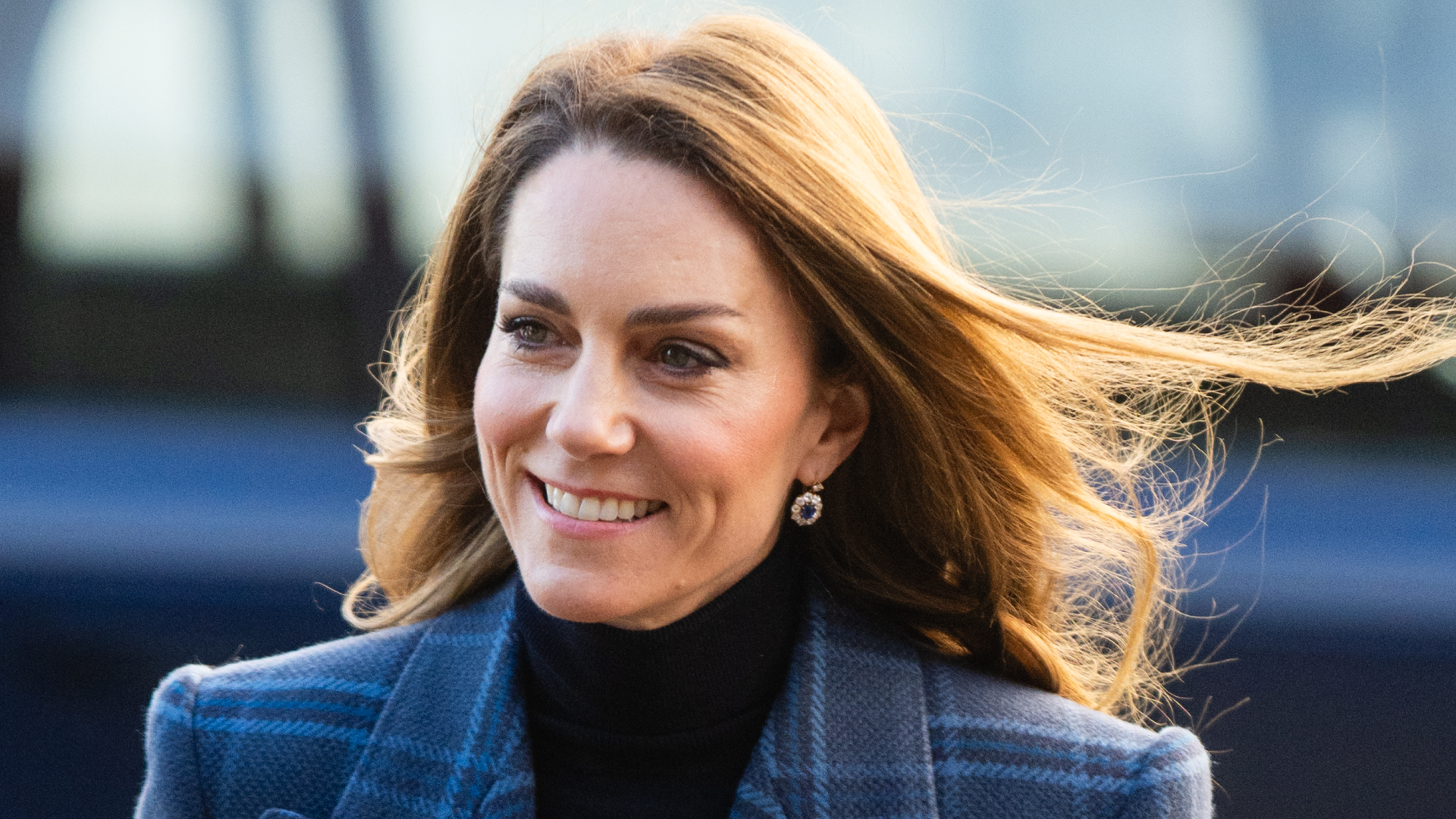 Kate Middleton smiling and wearing a blue tartan coat