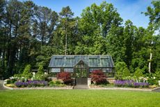 A large garden with a Victorian glasshouse and a backdrop of trees