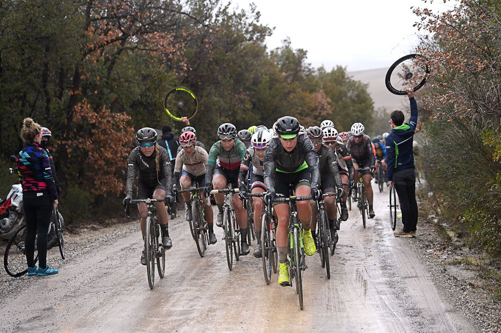 Mechanics wait with spare wheels for riders on the gravel of Strade Bianche