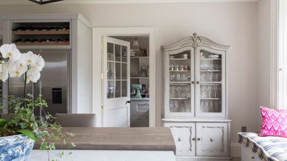 Dining room with antique cabinet holding glassware, looking into kitchen with shelves of china and blue mixer