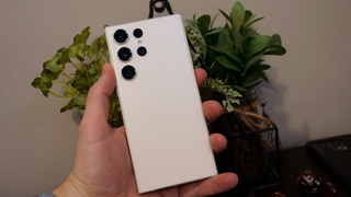 Back of cream colored Samsung Galaxy S23 Ultra held in front of a plant and a set of dice