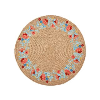 A round light brown jute placemat with light blue and red flower embroidery around the edges of it