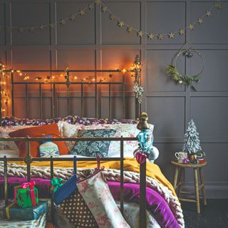 A wall-panelled bedroom decorated for Christmas with string lights hung on the bed headboard, star garlands and Christmas stockings