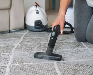 Woman cleaning a grey, low-pule carpet with a steam cleaner