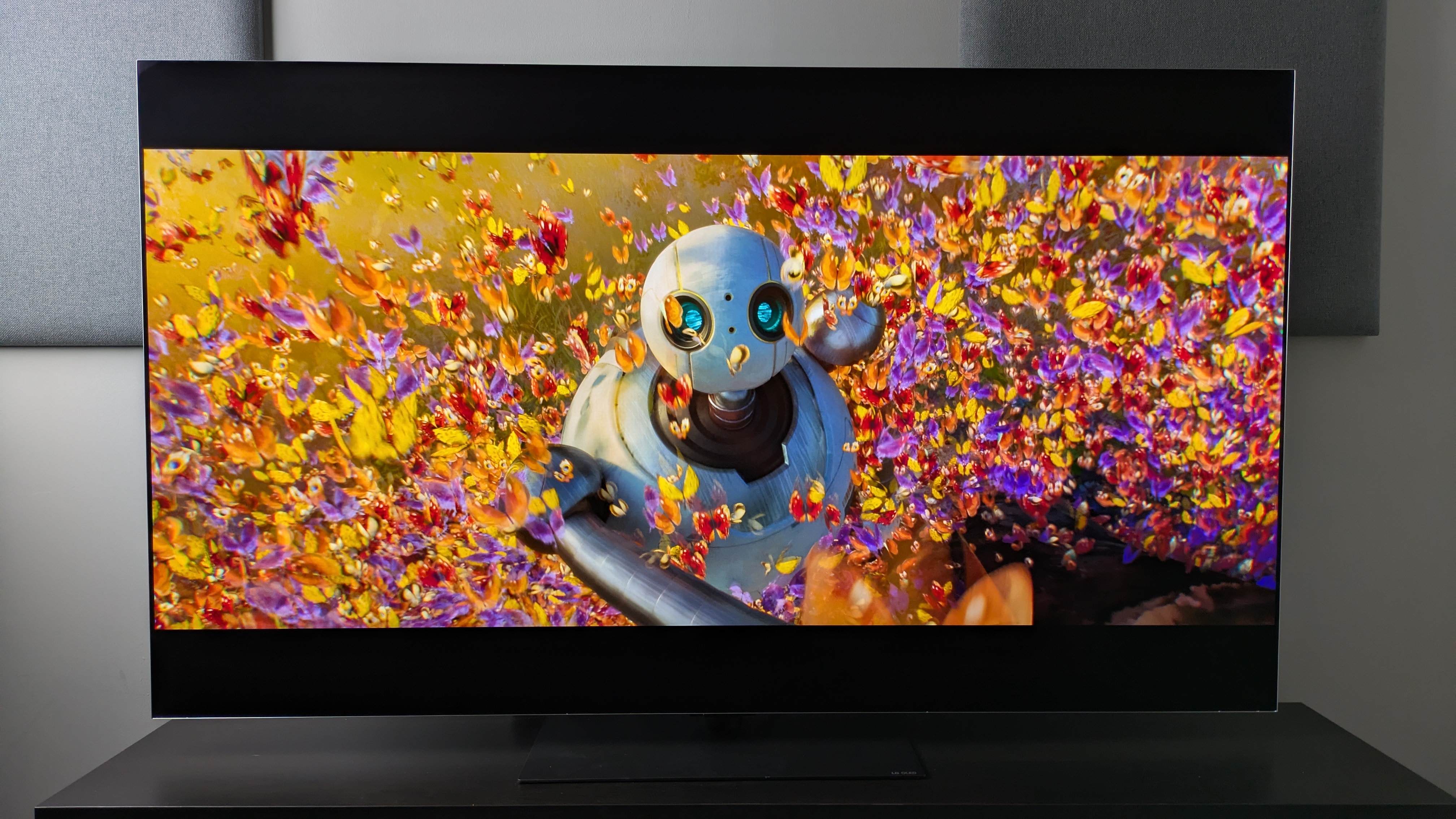 LG G6 OLED TV showing Roz from the Wild Robot surrounded by colorful butterflies. Demonstrates the G6's excellent color reproduction