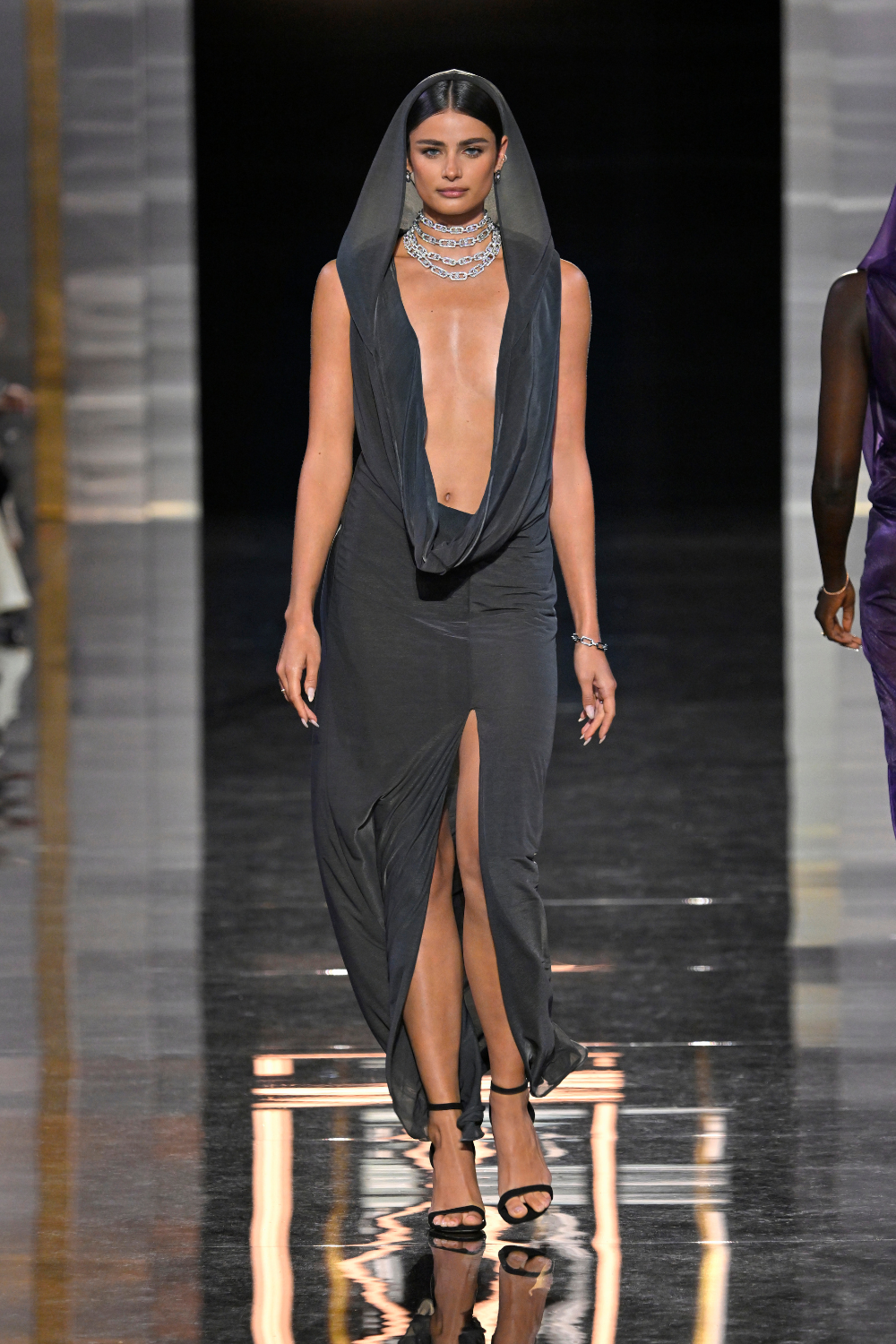 taylor hill walks down the runway with black hooded outfit and layered diamond necklaces