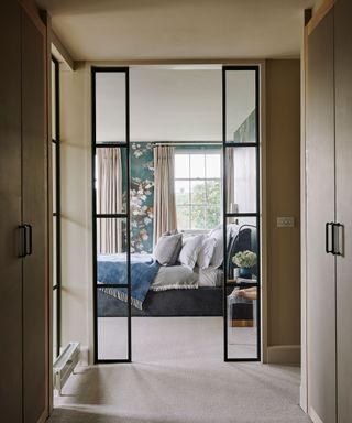 Walk-in closet ideas with glass doors leading into a neutral bedroom with blue patterned wallpaper.