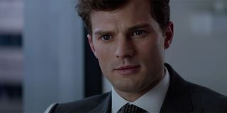 Jamie Dornan sitting in his office with a blue suit asking questions in Fifty Shades Of Grey trailer.