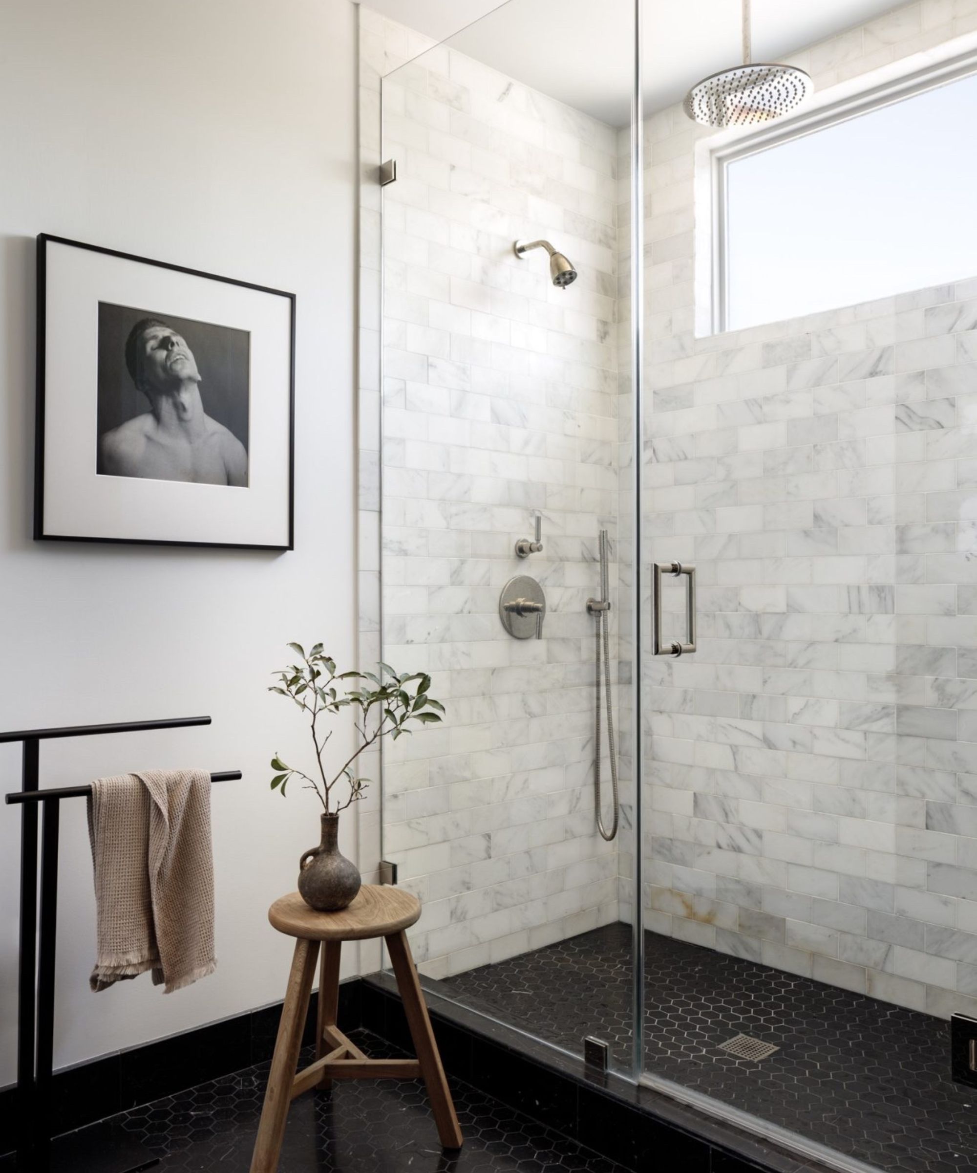 A minimalist bathroom with a black tiled floor, white walls, and marble shower tiles