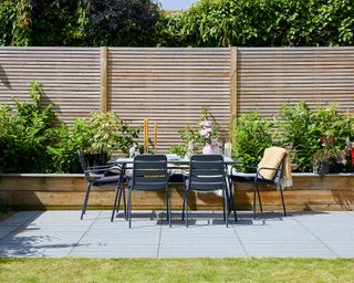 A wooden slat fence with raised planters in front is a backdrop to a modern outdoor dining area