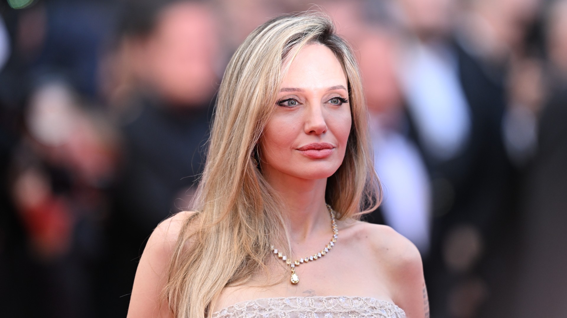 a woman with blonde hair photographed in front of a crowd of people on a red carpet