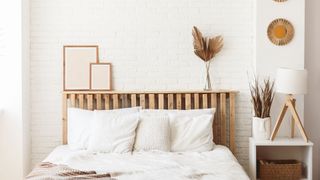 A bedroom with white brick walls, a wooden bedframe and white bedding on the bed, as well as wooden and white bedroom accessories.