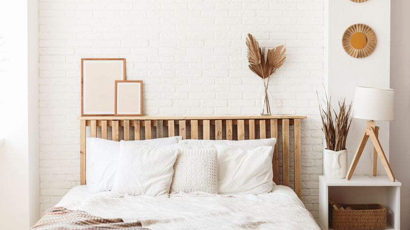 A bedroom with white brick walls, a wooden bedframe and white bedding on the bed, as well as wooden and white bedroom accessories.