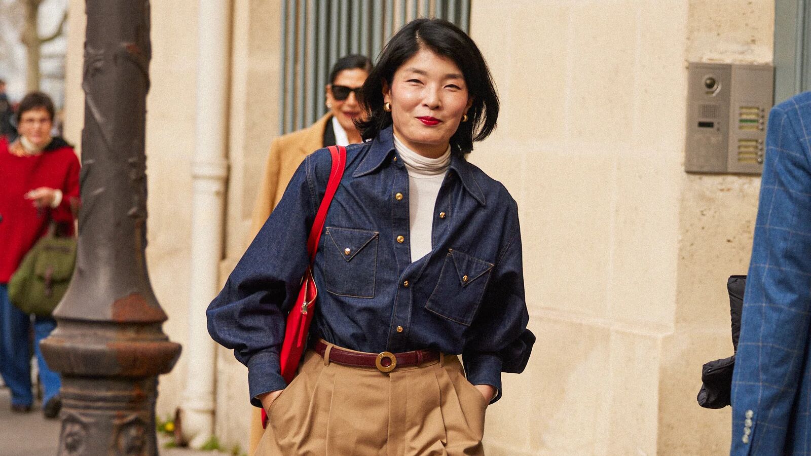 Woman wearing a denim button down, pleated shorts, white turtleneck, and a red bag