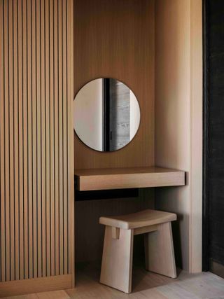 Wooden dressing table area in hotel with small stool and mirror