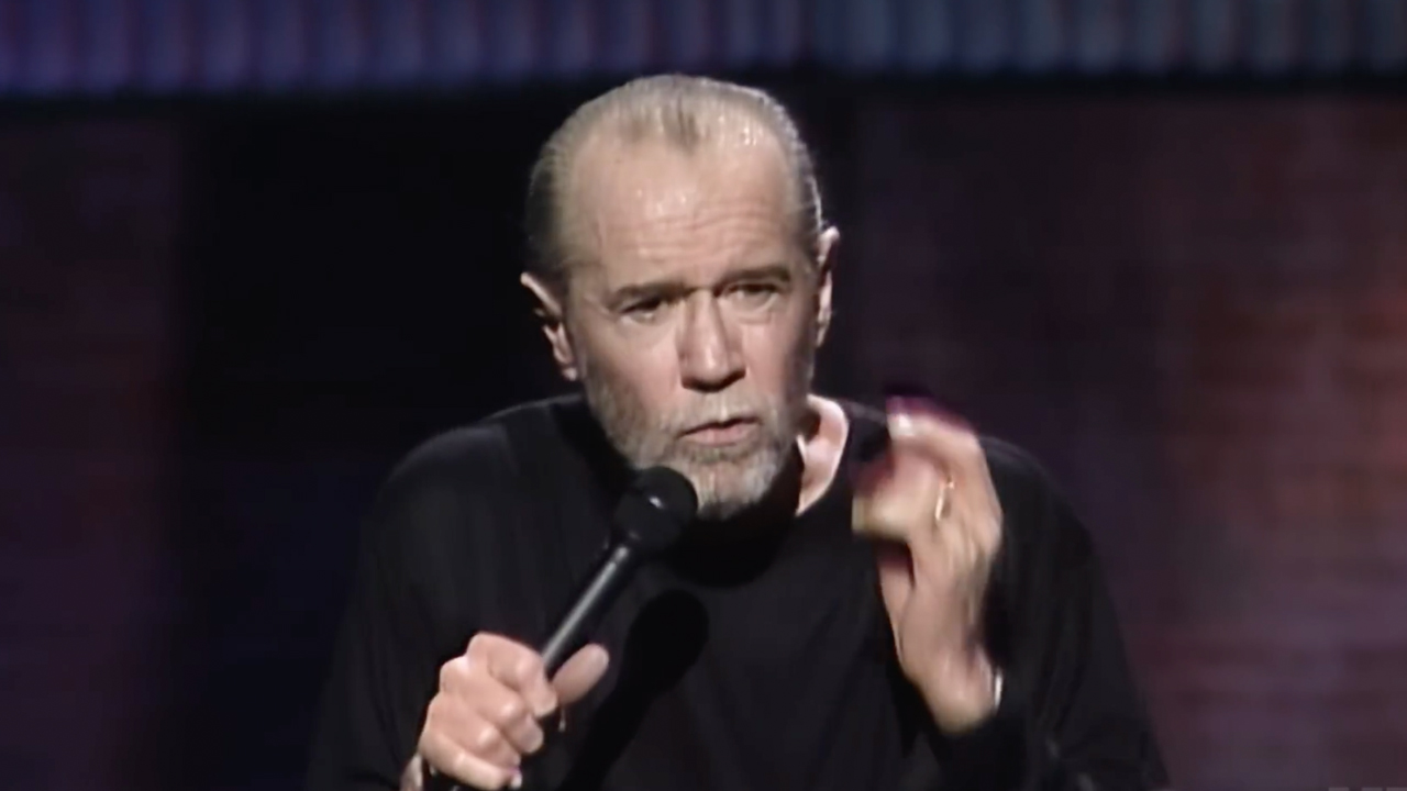 George dressed in black long sleeve shirt performing stand up featured in HBO's doc, George Carlin's American Dream.