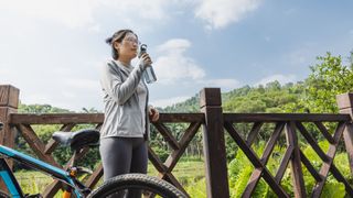 Woman holding up water bottle to drink, stopping on the side of a country road with bike