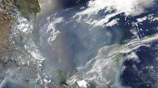 A spaceborne view of the Gulf, it looks hazy beneath smoke.