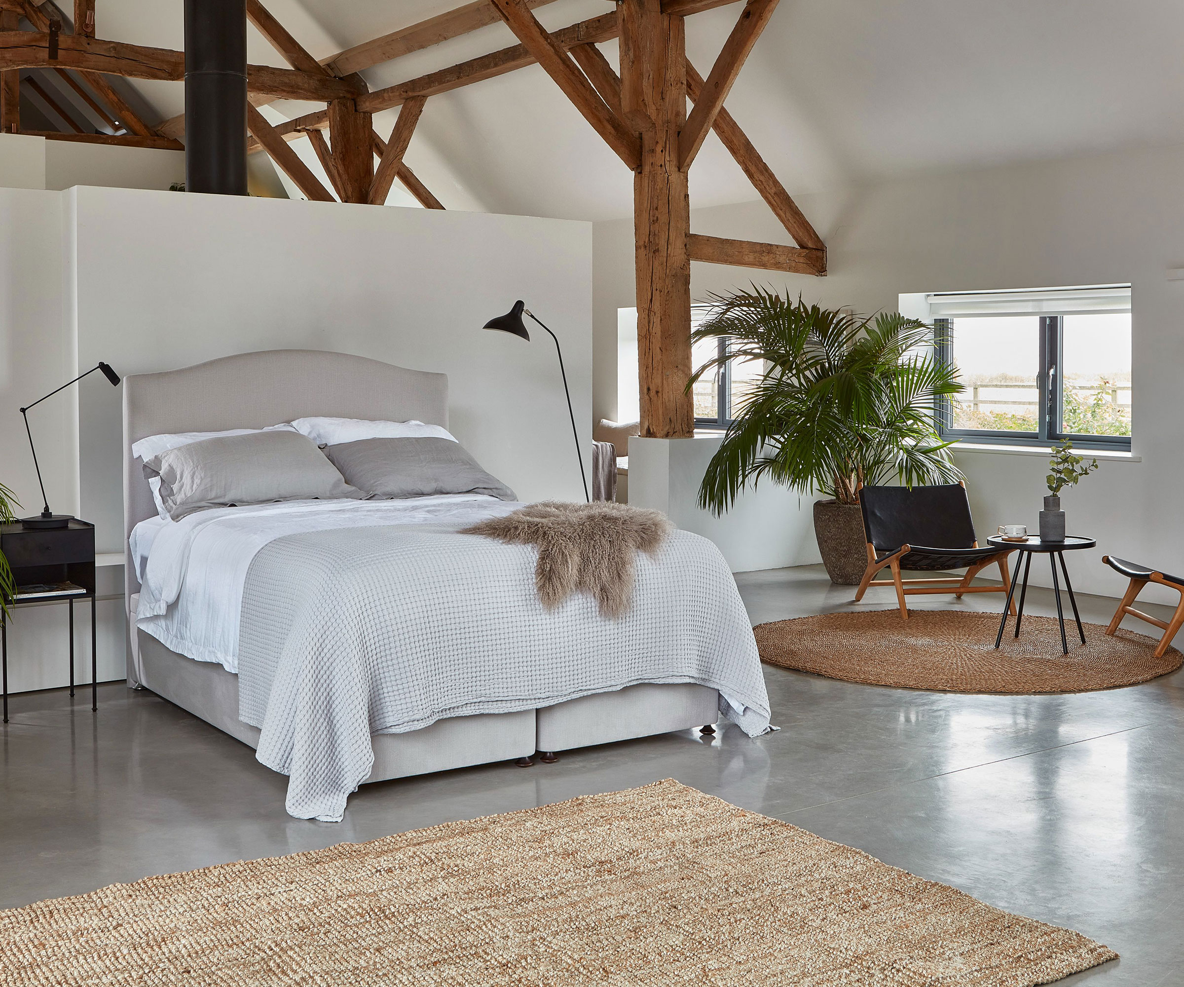 double bedroom in barn conversion with exposed beams and vaulted ceiling and polished concrete flooring