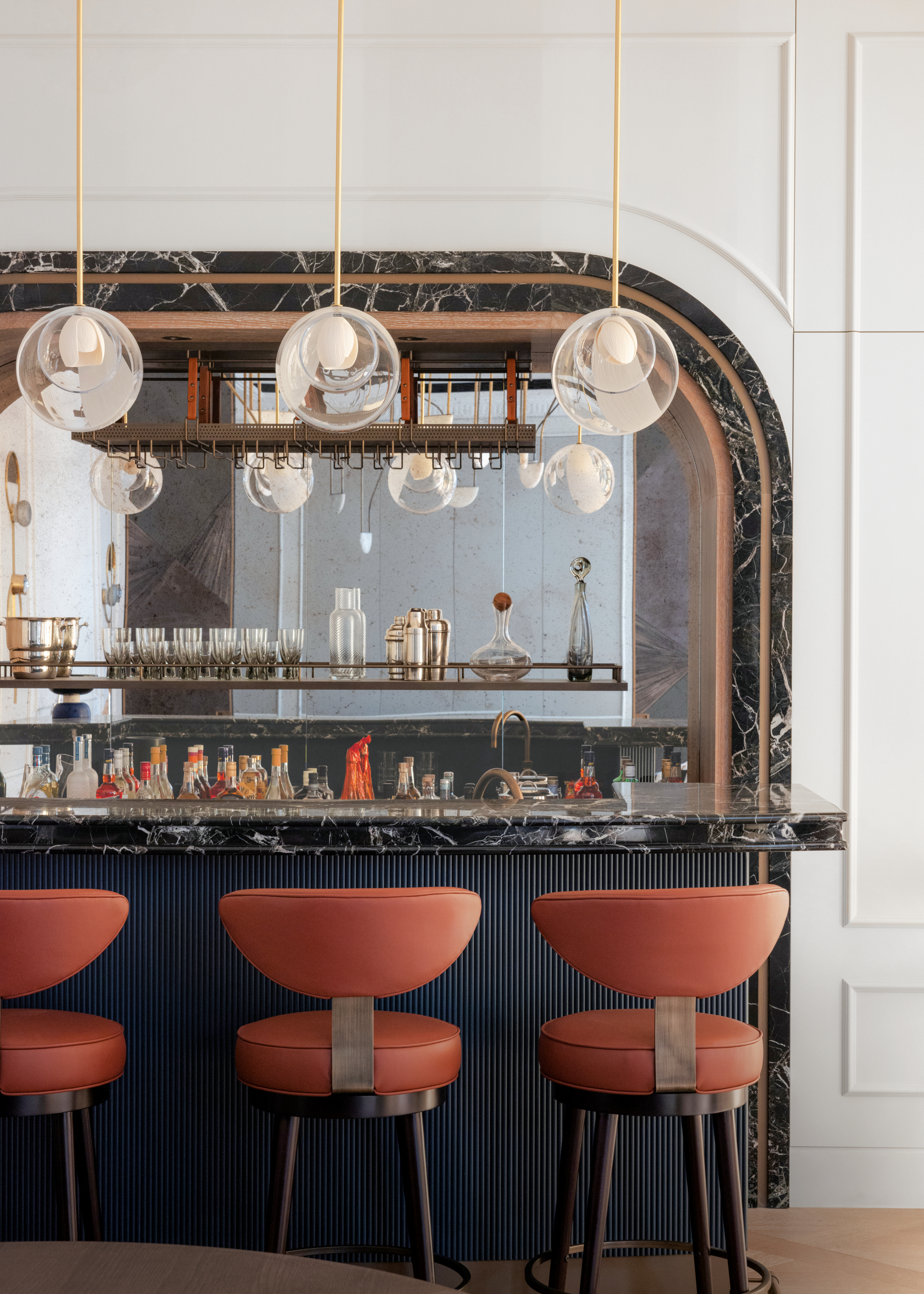 Home bar with black stone backdrop, navy ribbed island front, and orange-red bar stools