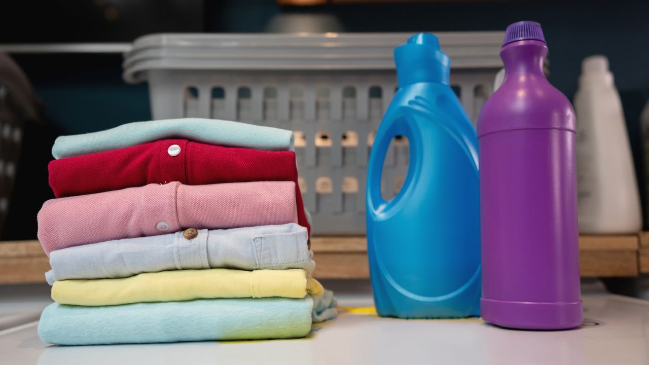 Folded multicolored polyester shirts on a washing machine next to laundry products — for article on how to wash polyester.