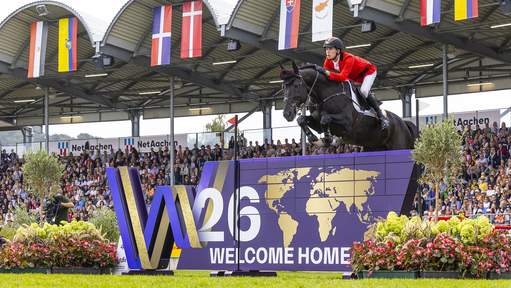 Thibeau Spits, a Belgian rider in a red coat, steers his black horse Impress-K Van&amp;rsquo;t Kattenheye Z over a purple decorated wall at the showjumping World Championships in Aachen