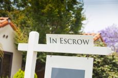 A sign reading "in escrow" on top of a "for-sale" sign at a house.