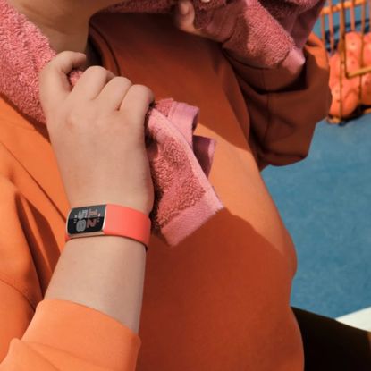 woman in an orange sweatshirt wearing a matching orange Google FitBit tracker