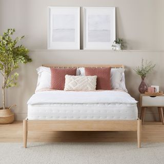 A mattress topper on top of a mattress on a wooden bed frmae with rust-coloured cushions