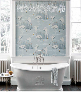 Ice and linen flamingo print wallpaper in a traditional bathroom with elegant tub, glass pendants and wooden flooring