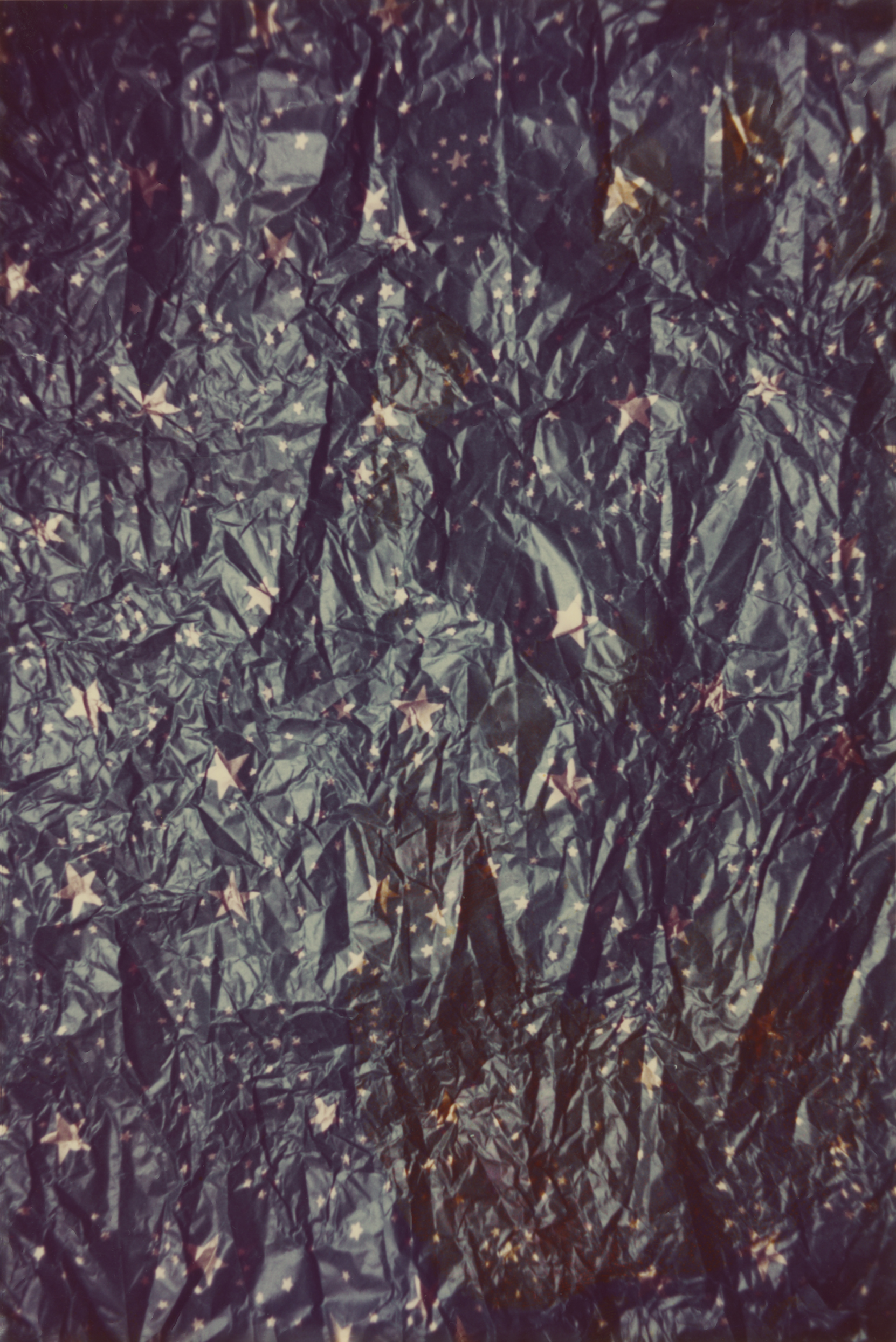 A crunched up, sheeny packaging paper foil with a blue background and golden stars, photographed up close from high up.