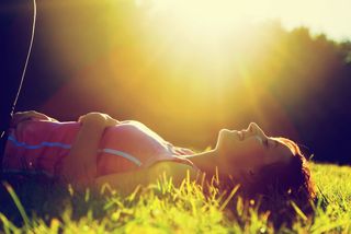 A woman lays on her back on the grass on a sunny day.