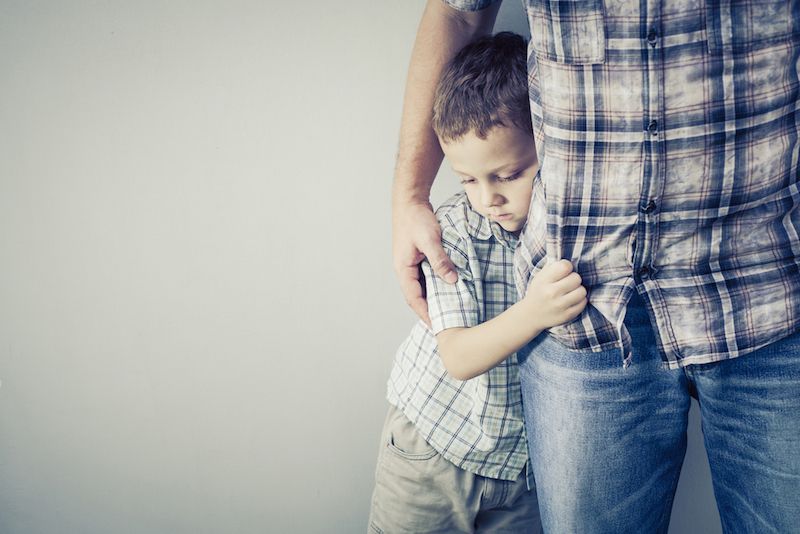 A shy boy clings to his dad.