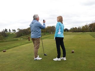 Jezz Elwood holding a rangefinder on the tee and talking to Alison Root