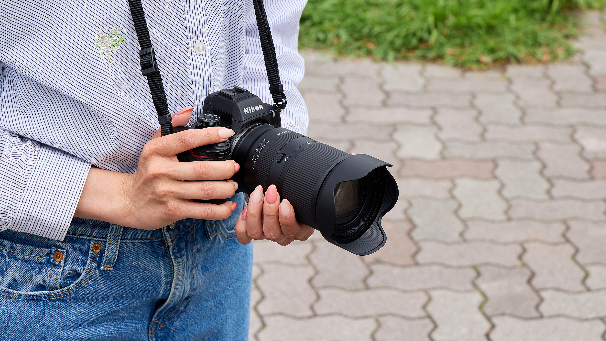 A lifestyle photo of the Tamron 18-300mm f/3.5-6.3 Di III-A VC VXD on a Nikon camera in a photographer's hands
