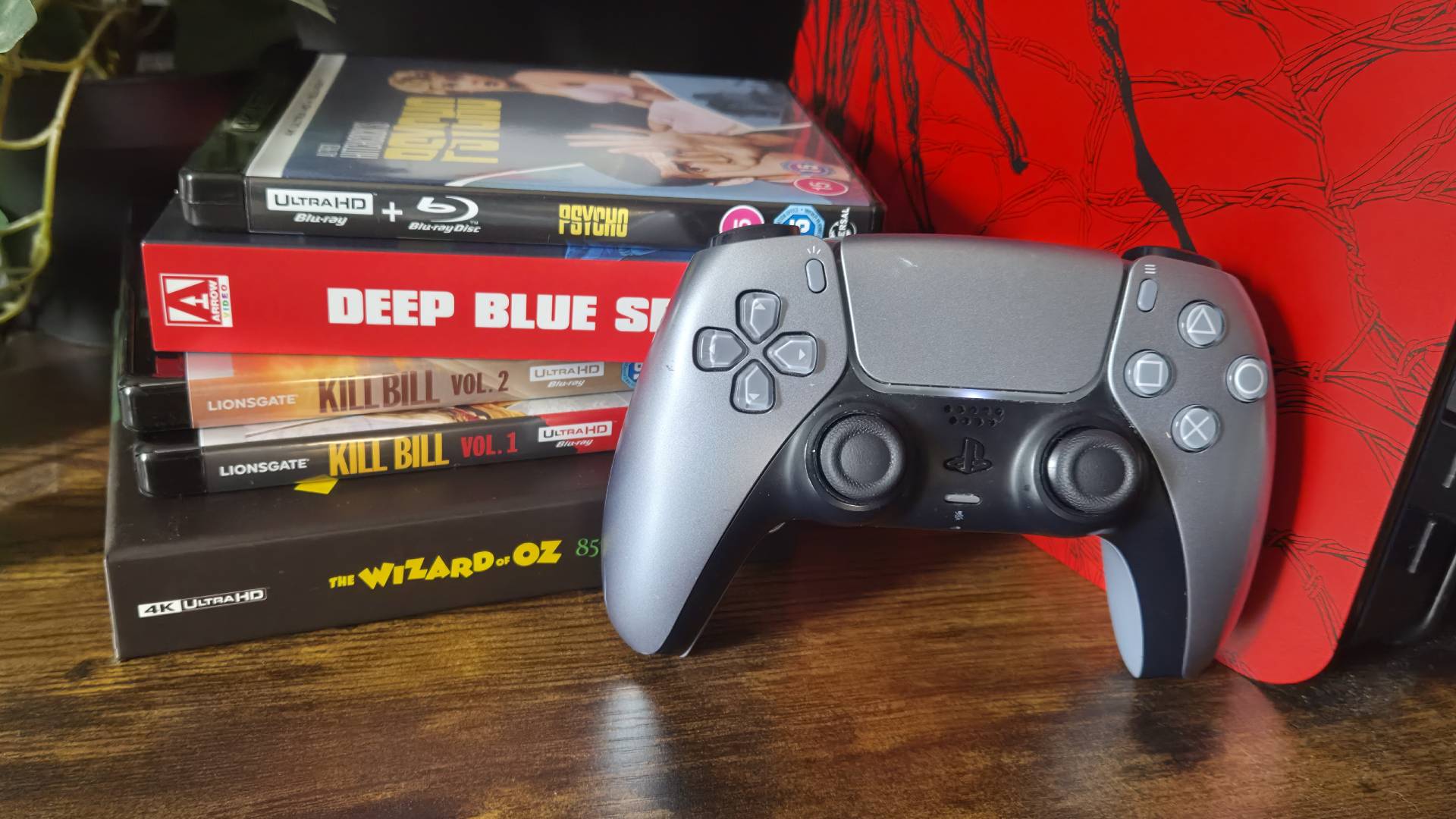 Photo of a silver PS5 DualSense controller sitting next to a pile of 4K Blu-rays.