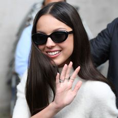 Olivia Rodrigo wears oval sunglasses while waving her hand to the crowd