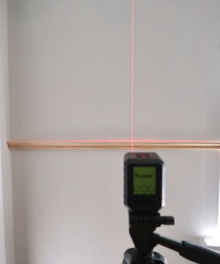 Huapar laser level on tripod with red beam shining on wall and wood molding decor