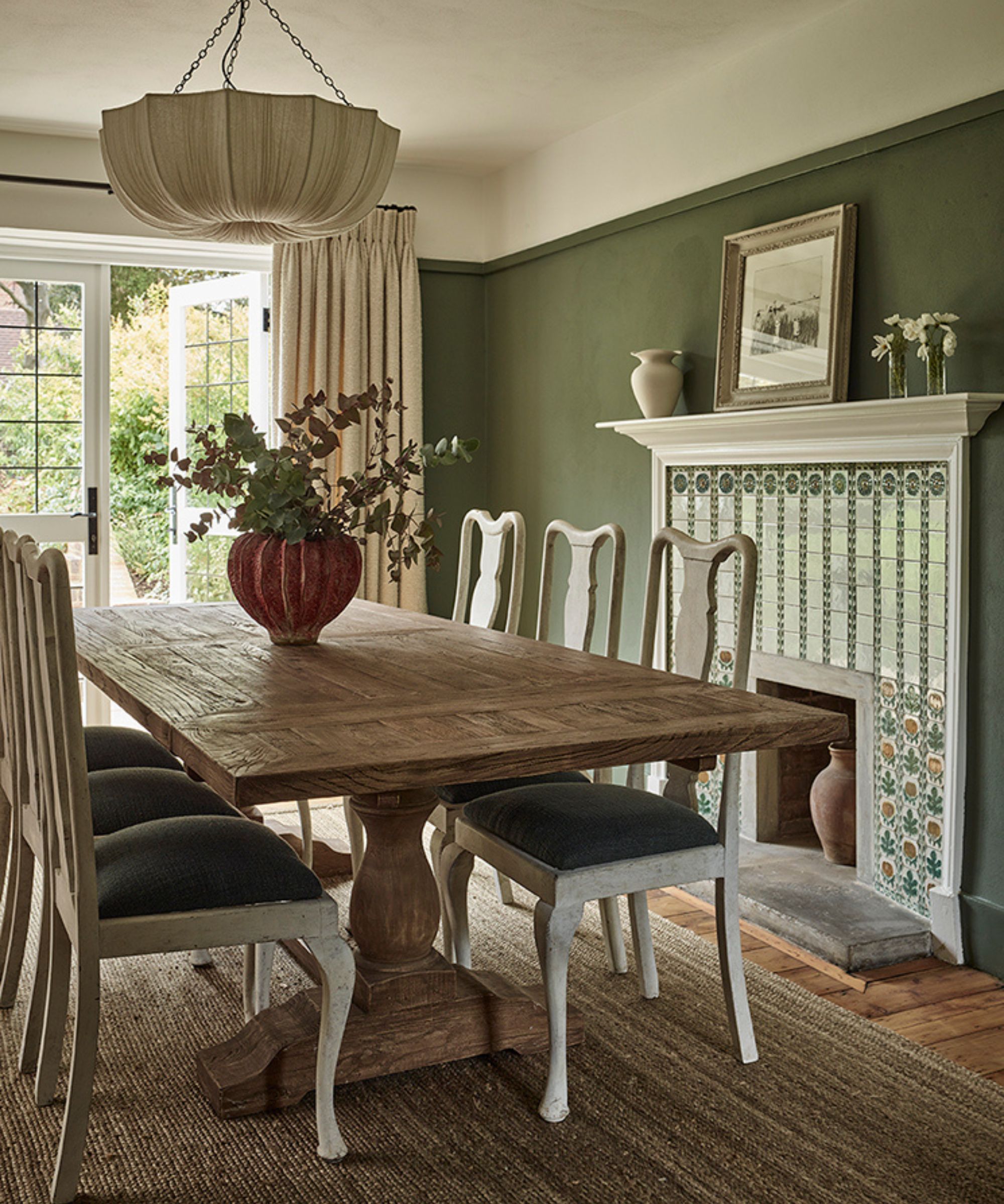a muted green dining room in a cottage in Hampstead with a fabric pendant light, rustic farmhouse table, and a original fireplace