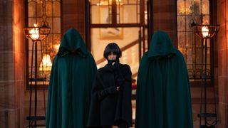Claudia Winkleman flanked by two hooded figures outside the castle for The Traitors season 2